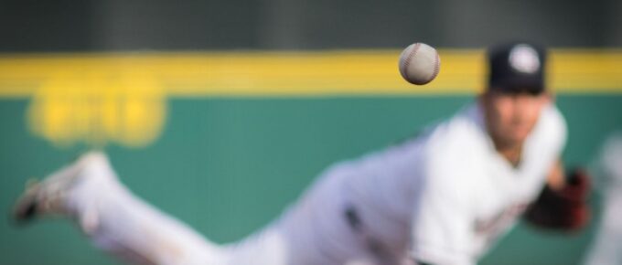 A baseball in motion with pitcher in background.