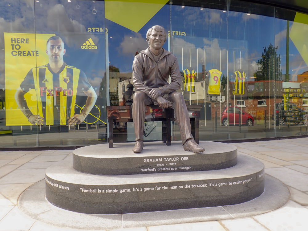 An image of a statue of Graham Taylor OBE, in front of the Watford FC Club Shop, Vicarage Road Stadium.