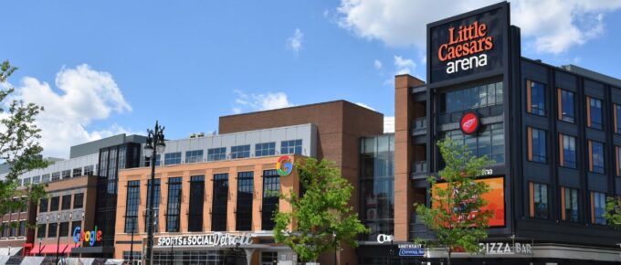 People walk past Little Caesars arena in Detroit, Michigan during the day.