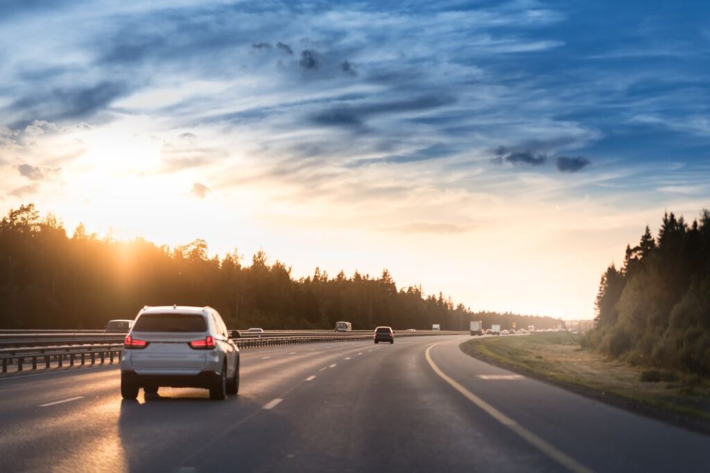 A road with metal safety barriers or rail and cars on the asphalt under the cloudy sky.